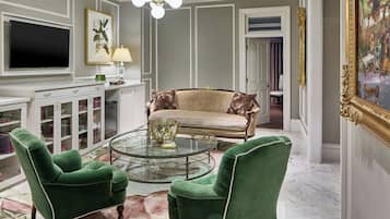 A living room with a green armchair, a sofa, a glass coffee table, a TV, a lamp, and a painting.