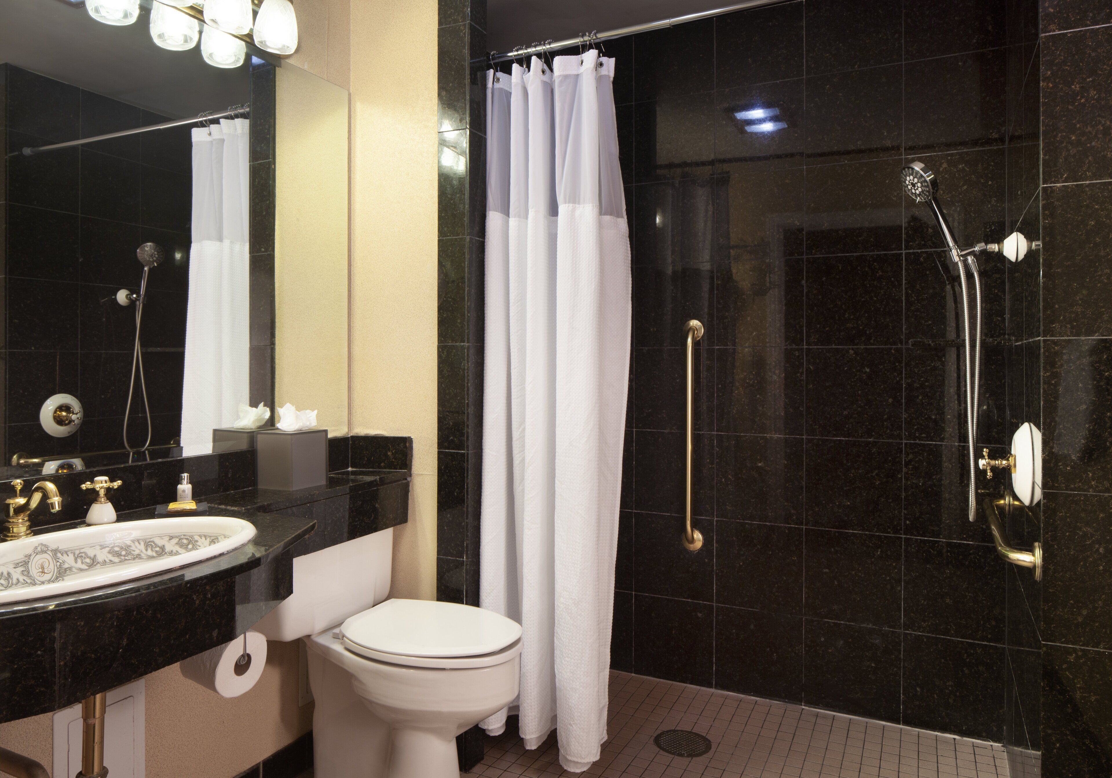 A modern bathroom with a black tiled wall, a white toilet, a sink with a gold faucet, and a shower with a handheld showerhead.