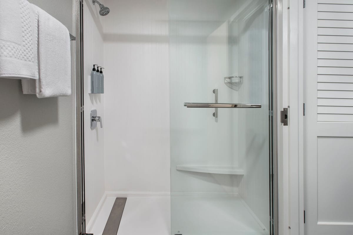 Ein modernes Badezimmer mit Duschkabine aus Glas, einem weißen Handtuch an der Wand und einer kleinen Ablagefläche mit Pflegeprodukten.
