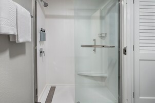 Un baño moderno con cabina de ducha de vidrio, una toalla blanca colgada en la pared y un pequeño estante con artículos de tocador.