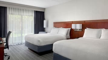 A hotel room with two beds, a desk, and a chair.