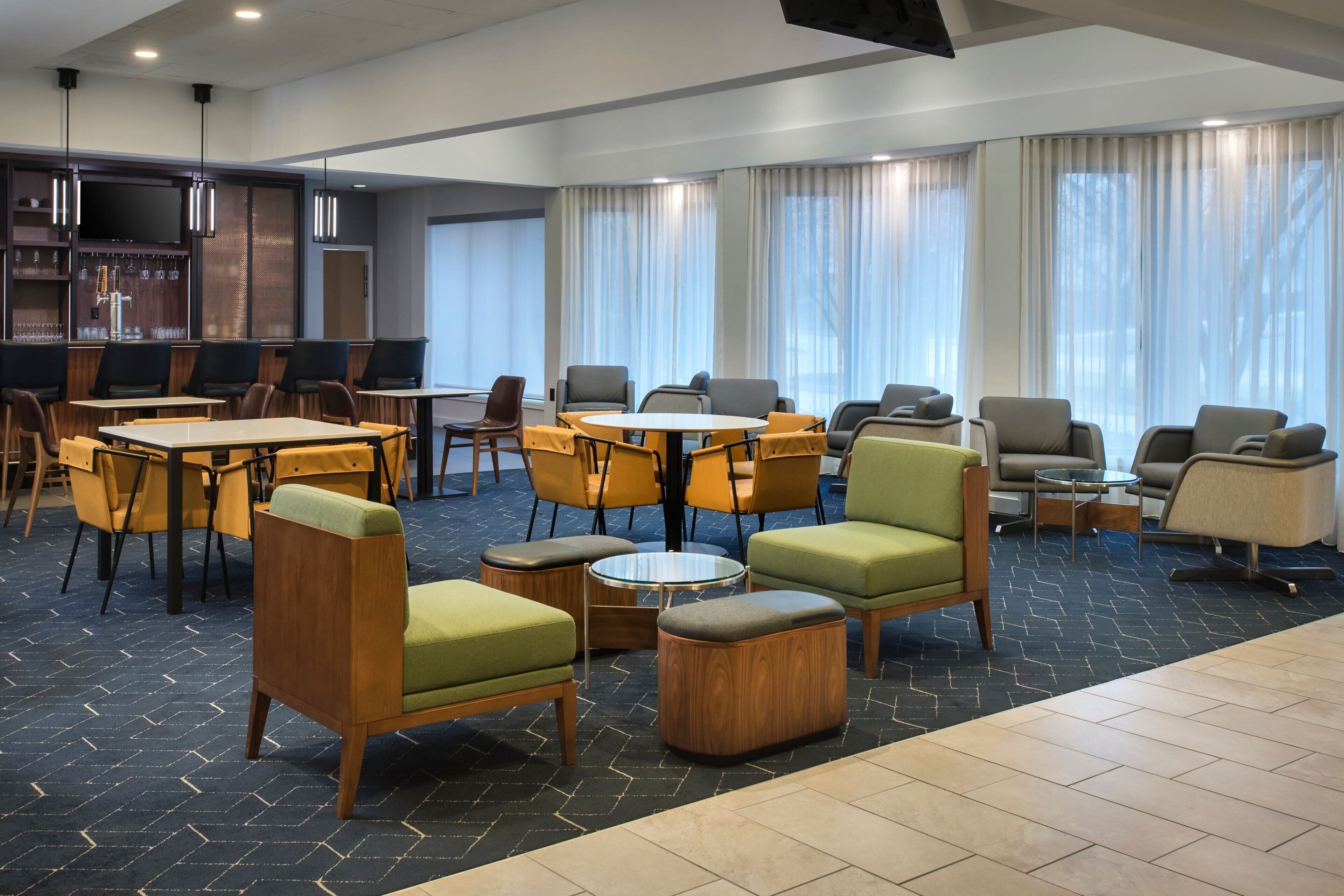 A hotel lobby with multiple seating areas, including tables and chairs, and a bar area with a television.