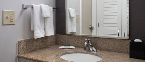 A bathroom with a granite countertop, a sink, a mirror, a towel rack, and a door.