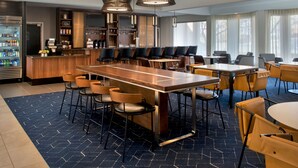 Un hall d’hôtel moderne doté d’un bar central, de différents espaces aménagés pour s’asseoir et d’une grande fenêtre laissant entrer la lumière naturelle.