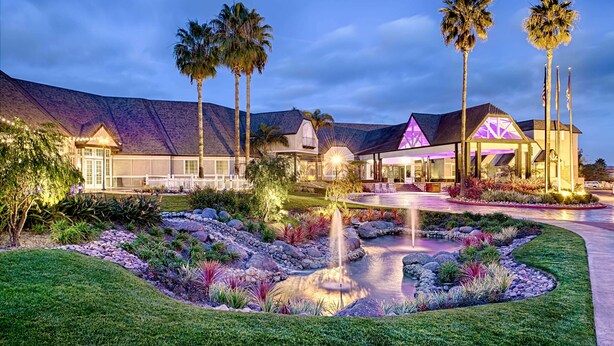 A modern hotel with a landscaped garden, palm trees, and a well-lit entrance.