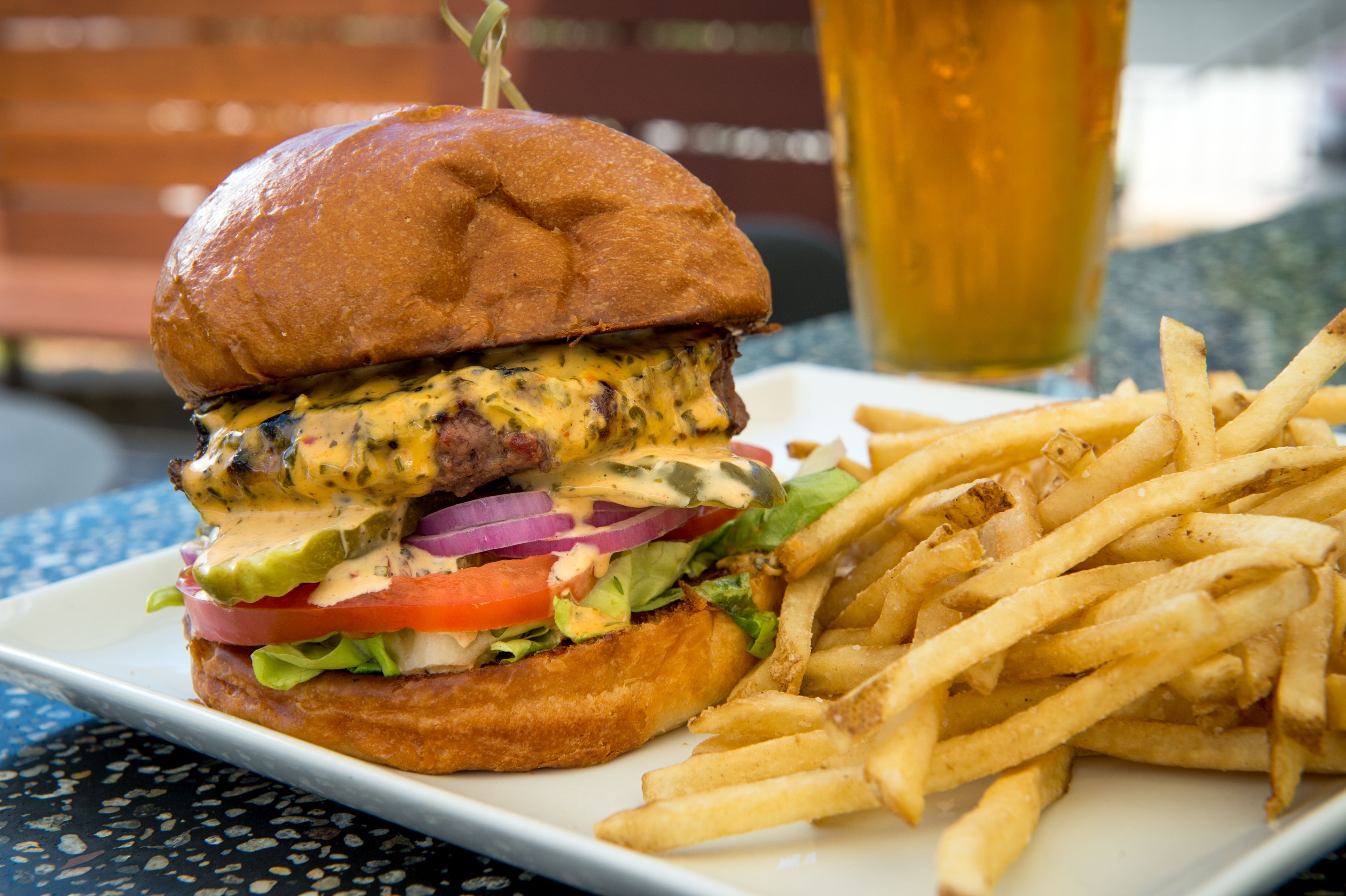 A burger with a side of fries and a glass of beer on a table.