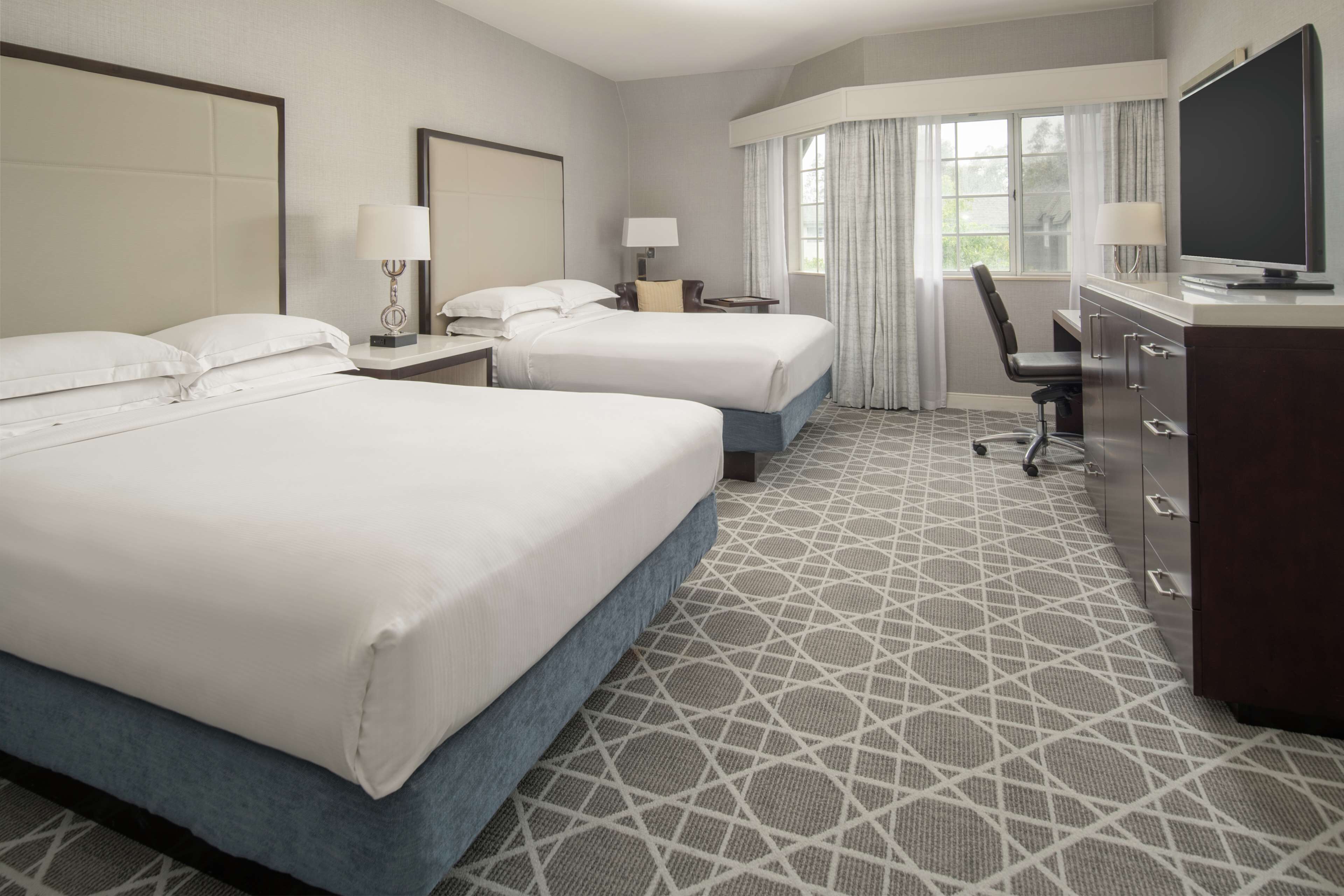 A hotel room with two beds, a desk, a chair, a TV, and a dresser.