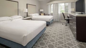 A hotel room with two beds, a desk, a chair, a TV, and a dresser.