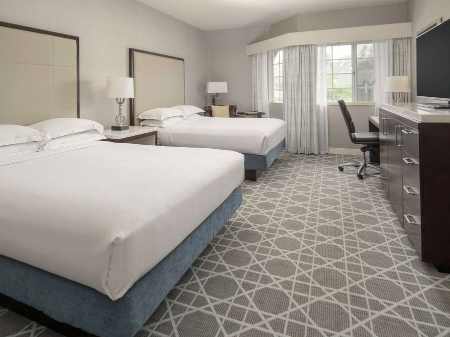 A hotel room with two beds, a desk, a chair, a TV, and a dresser.