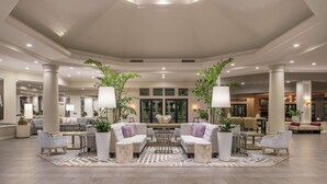 A spacious lobby with a central seating area, large columns, and potted plants.