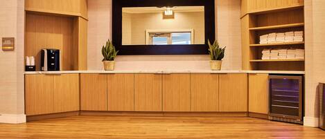 Un moderno hall de hotel con piso de madera, un espejo grande, una máquina de café y una vitrina refrigerada.