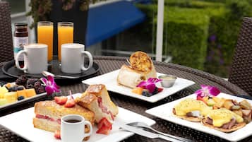 Una escena de desayuno con diversos platos, incluyendo tostadas, panqueques y huevos, sobre una mesa con vista a un jardín.