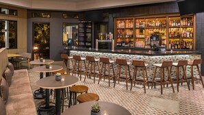 A bar area with a variety of seating options including round tables and bar stools, a bar counter with a display of bottles, and a patterned floor.