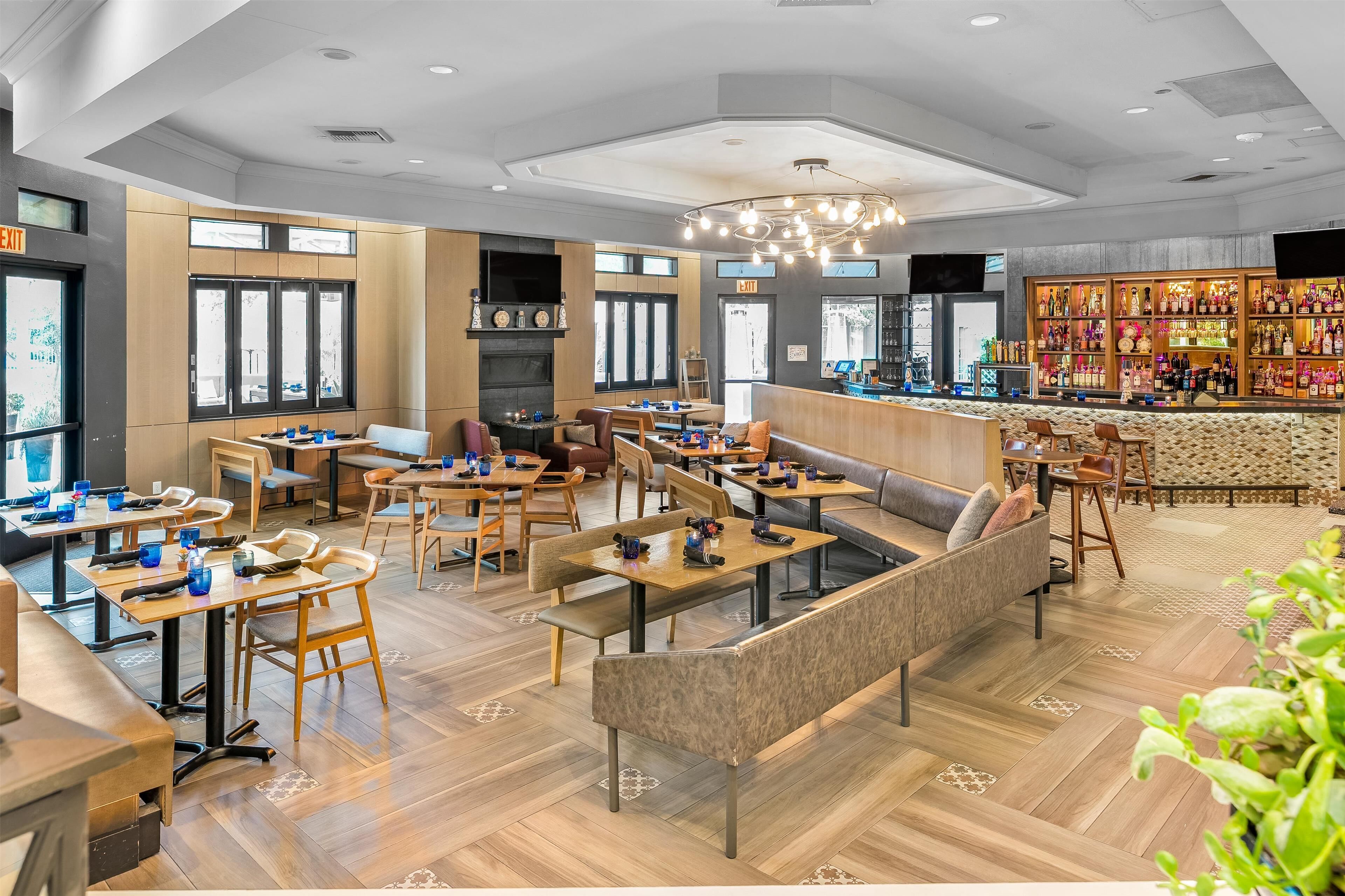En rymlig hotellobby med flera sittgrupper, en bar med ett stort utbud av spritflaskor och stora fönster som släpper in naturligt ljus.