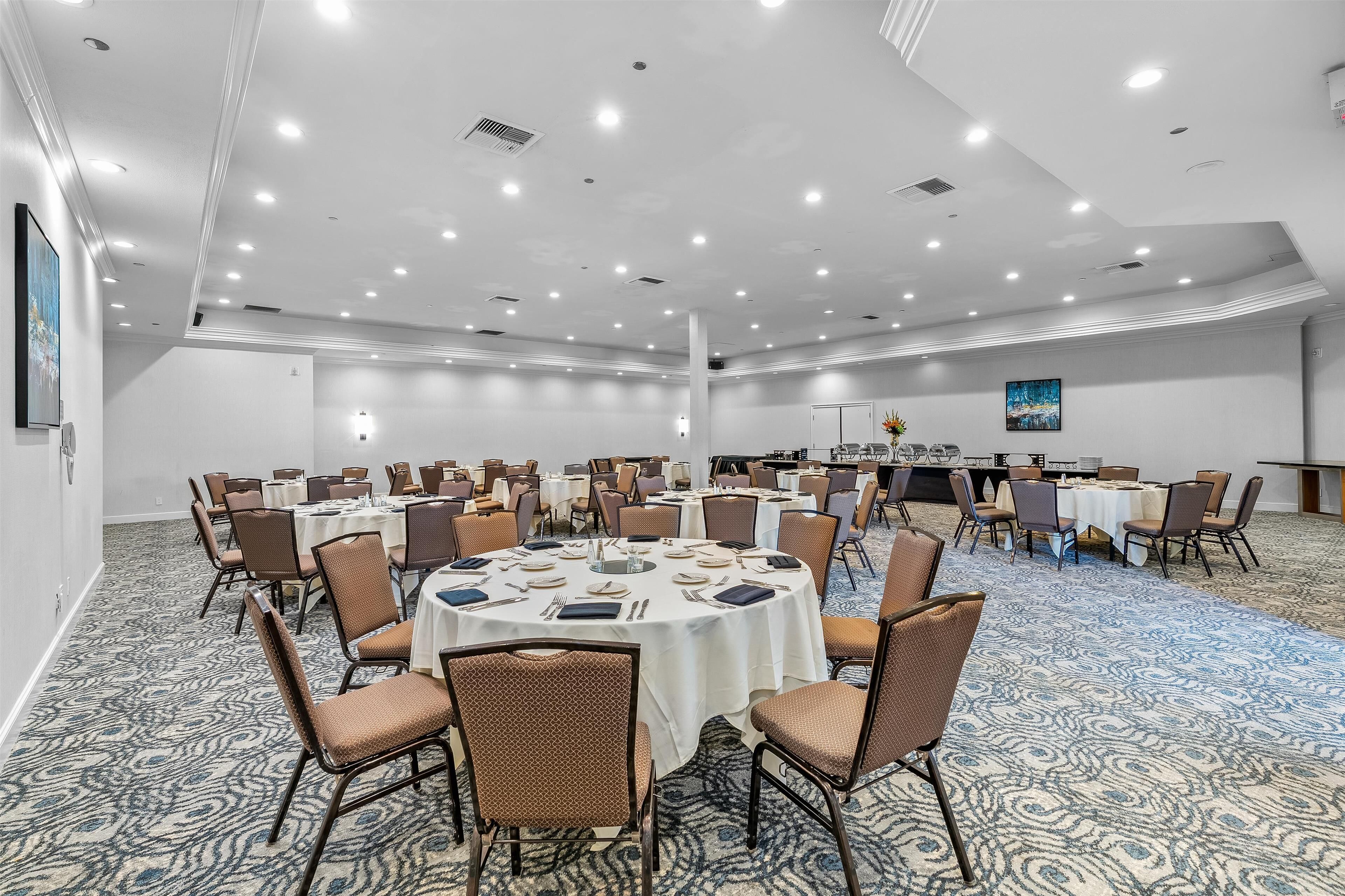 A large conference room with round tables, brown chairs, and a carpeted floor.