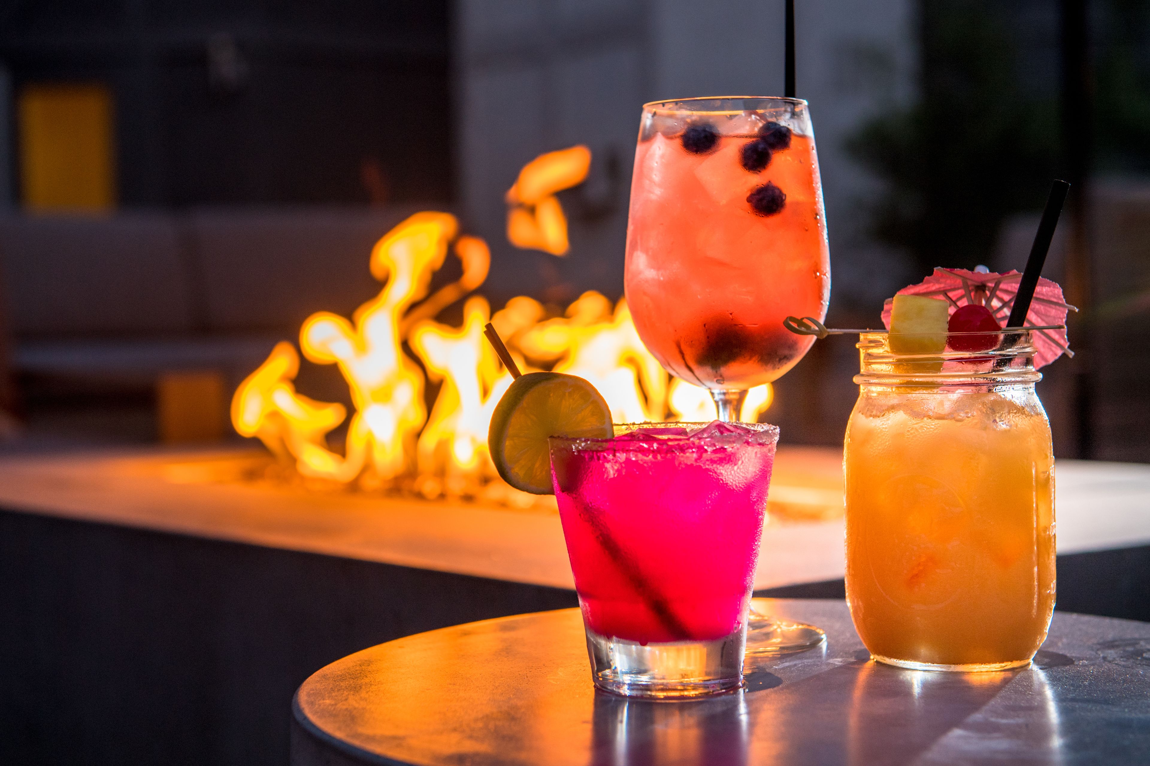 Two cocktails on a table with a fire in the background.
