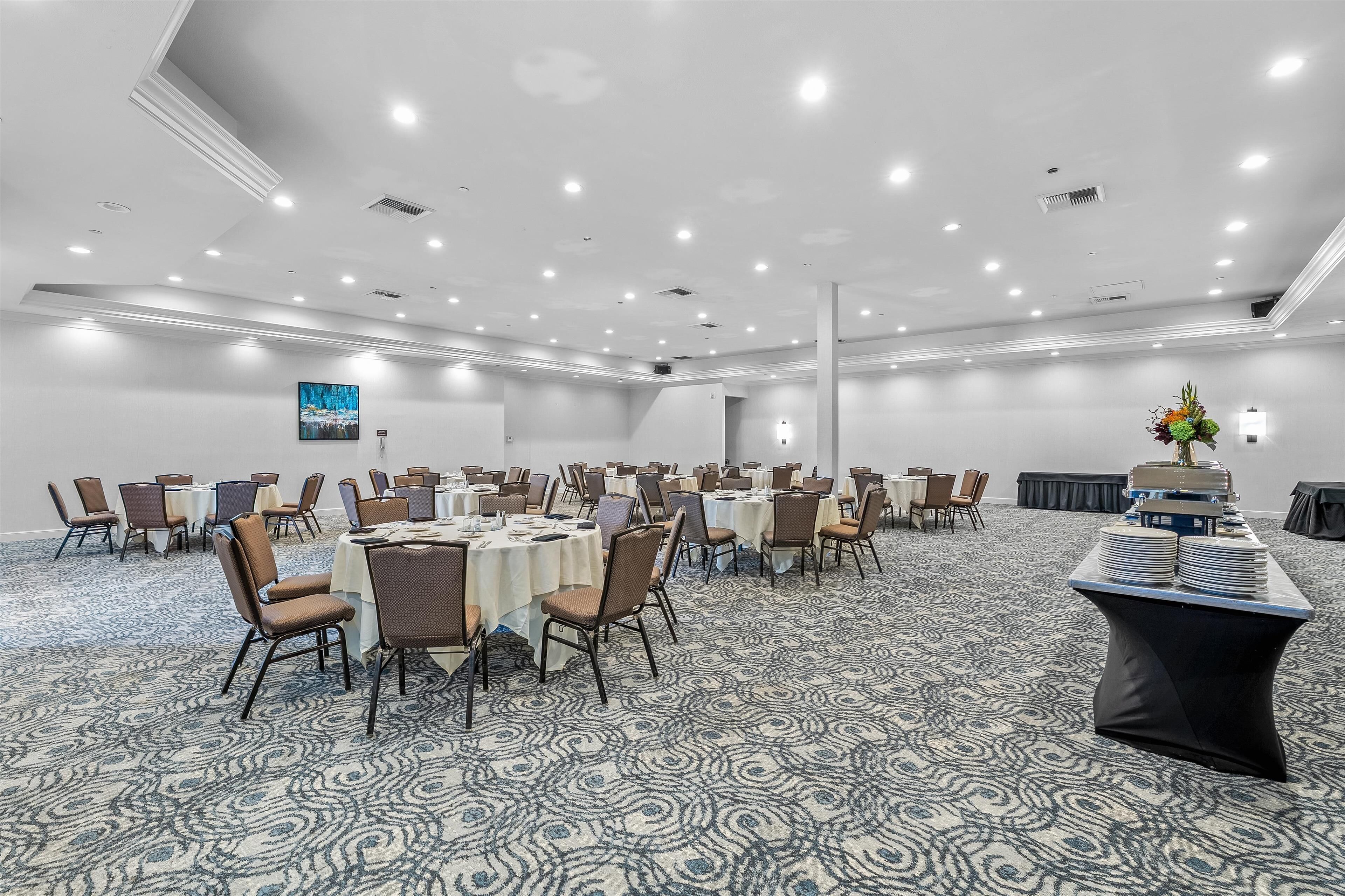 Une grande salle de conférence dotée de tables et de chaises rondes, d’un sol recouvert de moquette et d’un plafond pourvu d’un éclairage encastré.