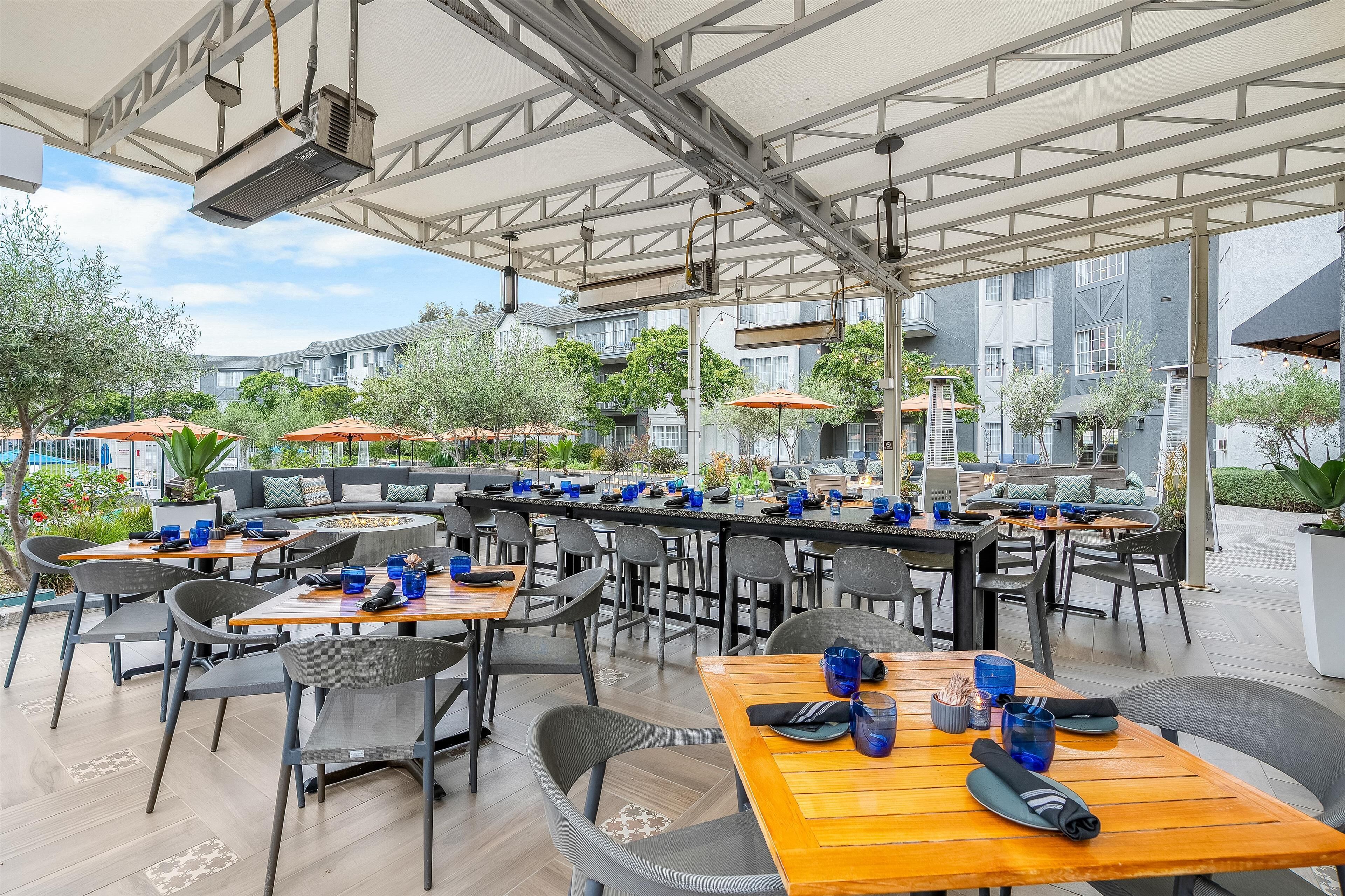 Een buitenterras met meerdere tafels en stoelen, een bar en parasols.