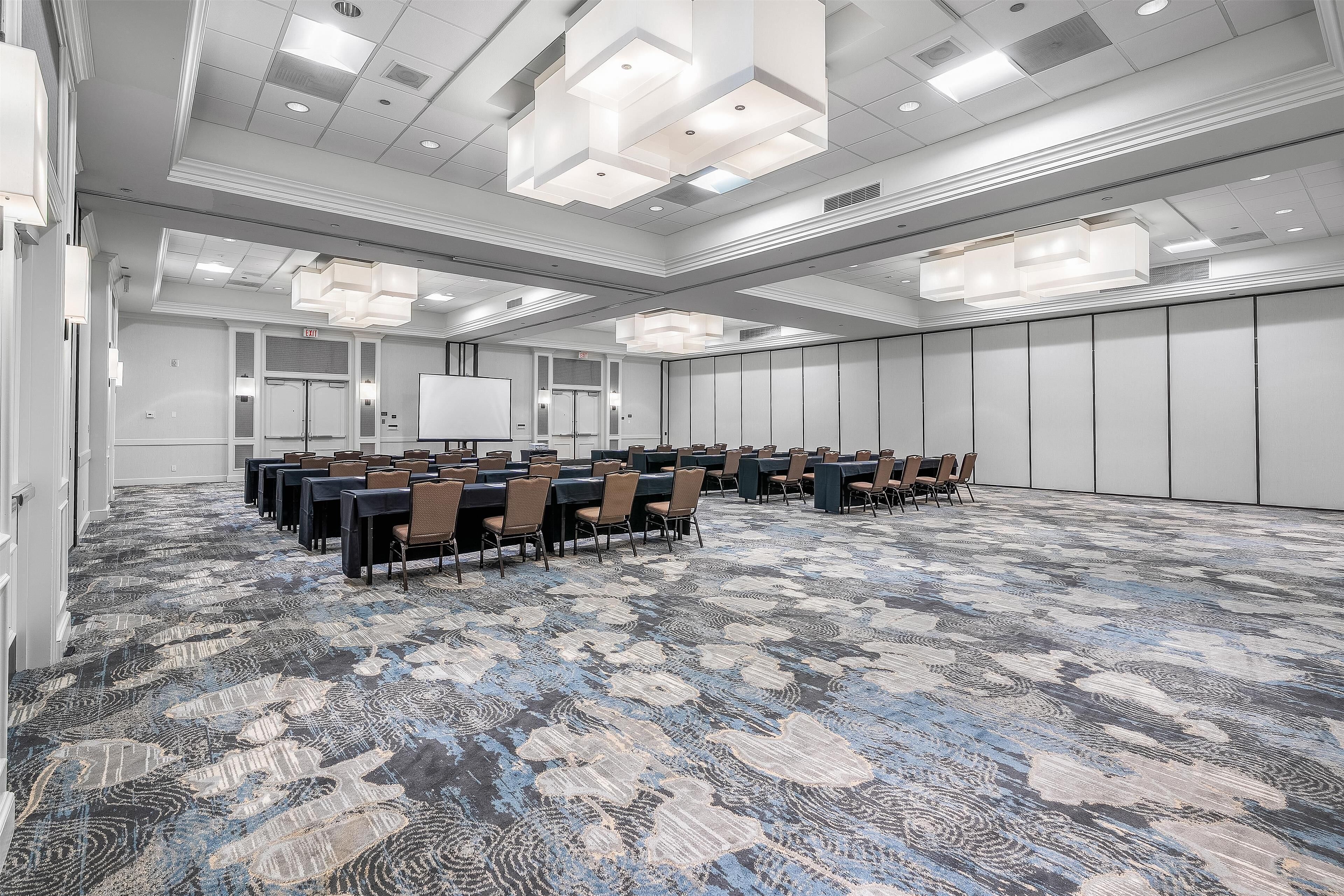 Un salón de conferencias con alfombra estampada, paredes blancas e iluminación empotrada en el techo.