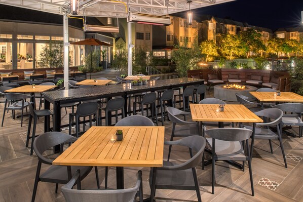 An outdoor dining area with multiple tables and chairs, a bar, and a fire pit.