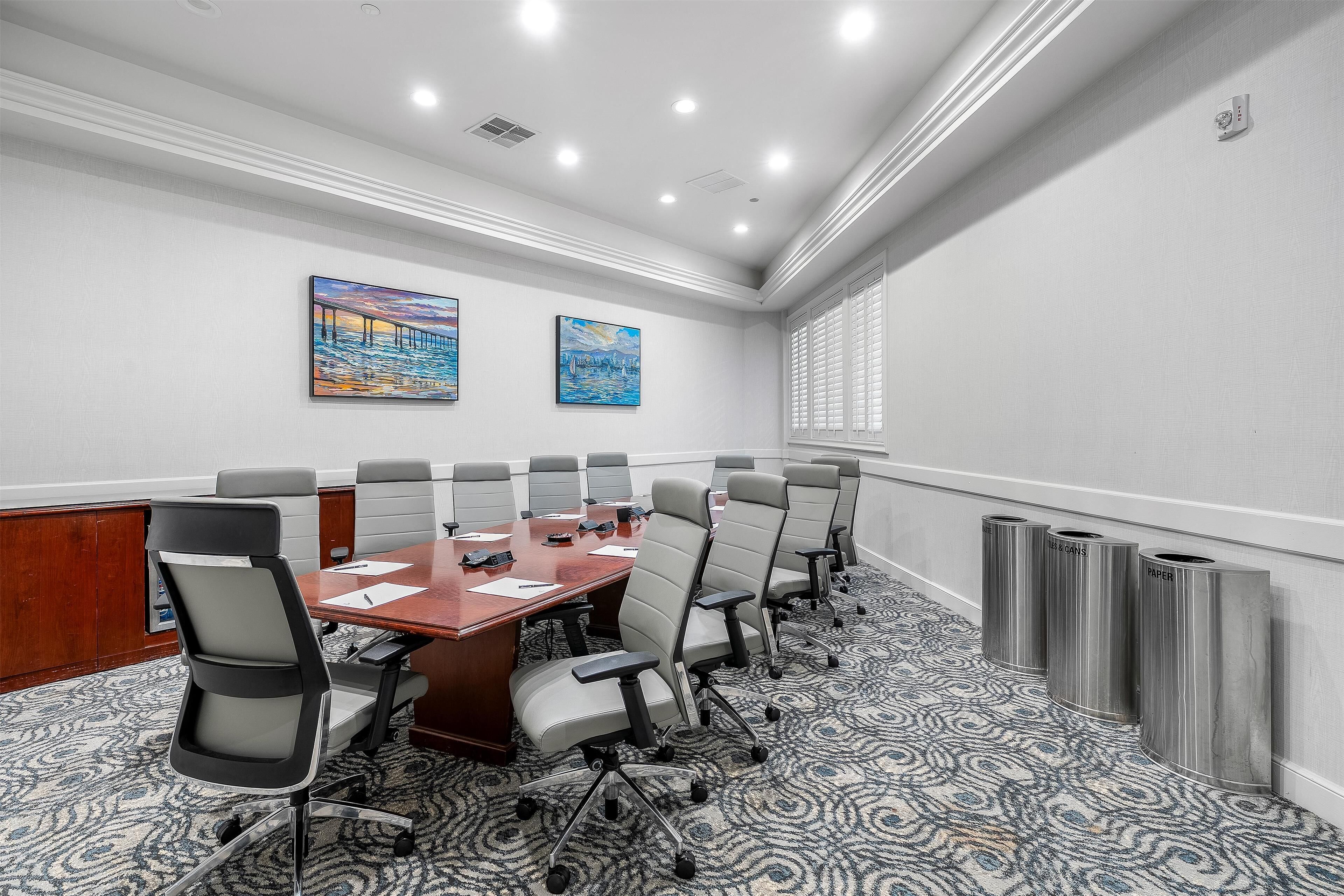 A conference room with a long table, multiple chairs, and two paintings on the wall.