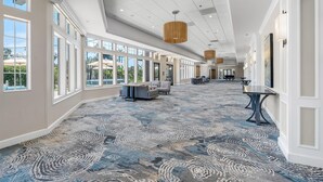 A spacious hotel corridor with large windows, a patterned carpet, and modern lighting fixtures.
