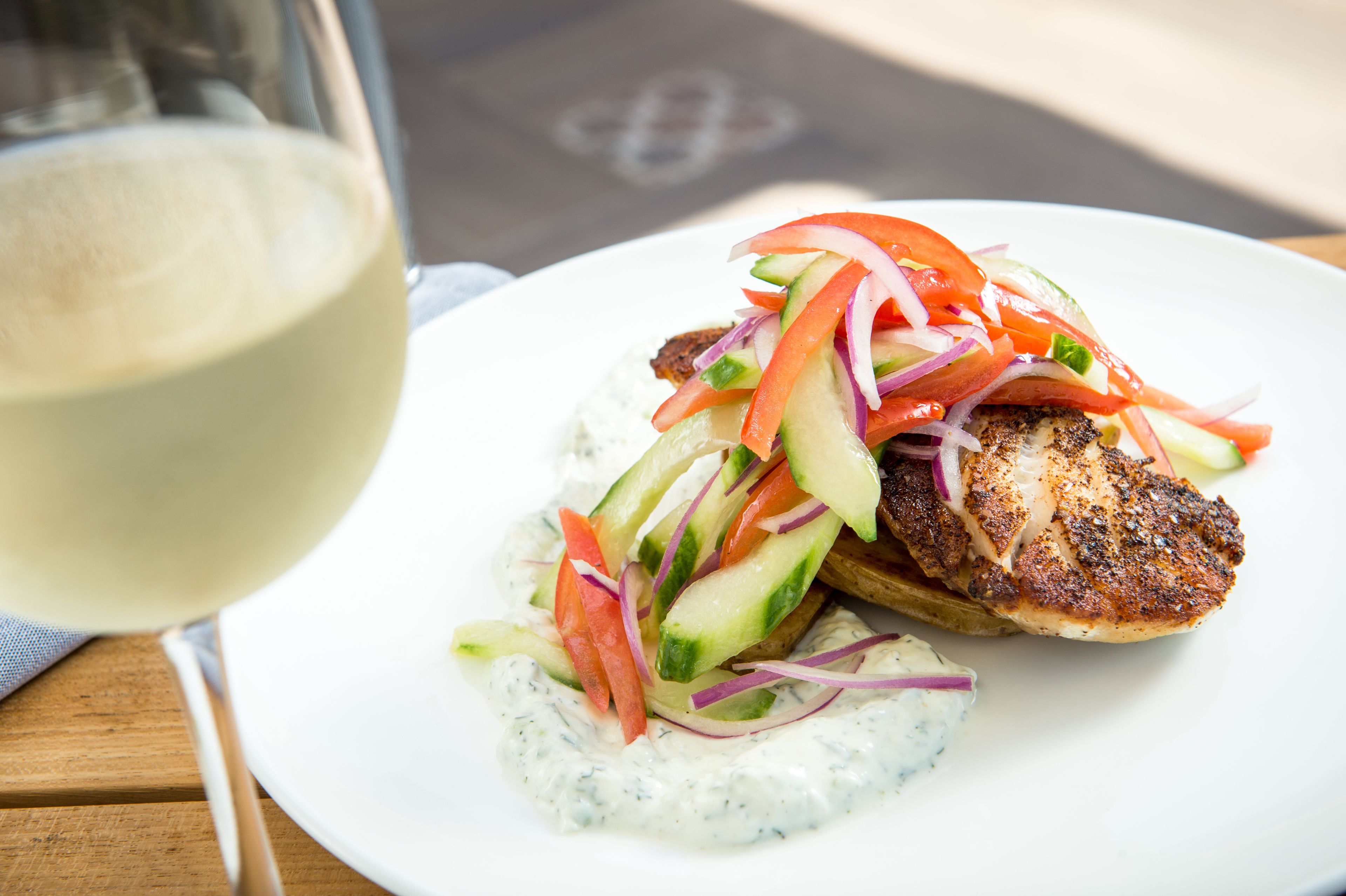 Grillet kylling med en salat og et glas hvidvin på et træbord.