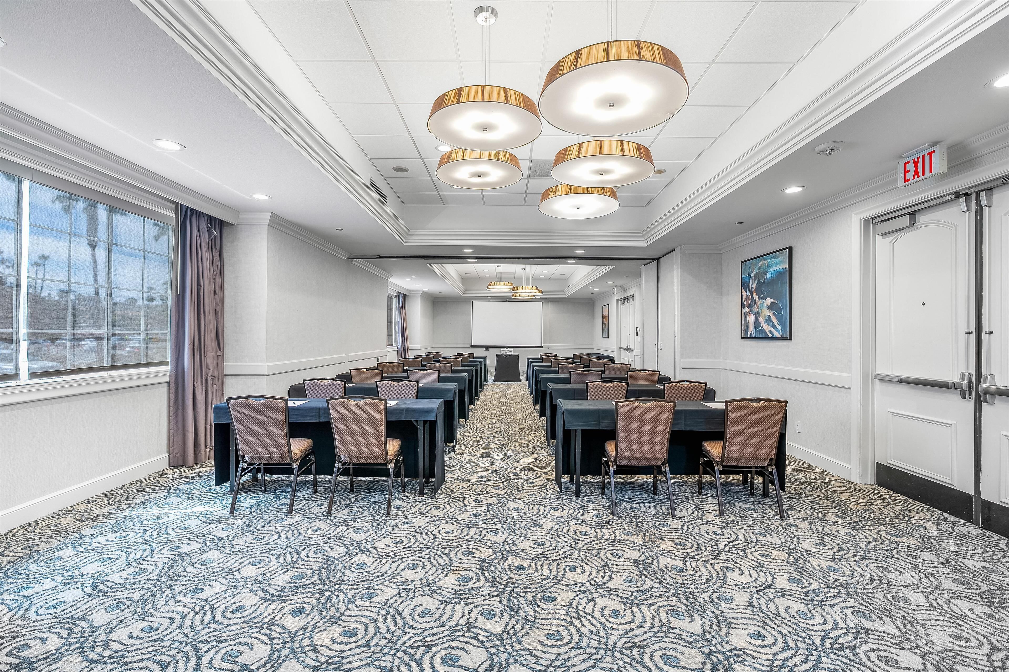 A conference room with a patterned carpet, rows of tables and chairs, and pendant lighting.