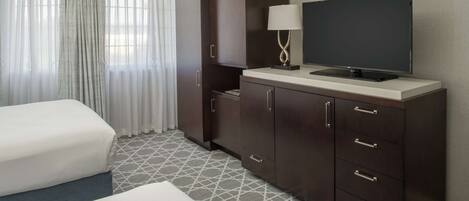 A hotel room with a bed, a TV on a cabinet, and a window with curtains.