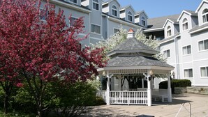 A gazebo with a white roof and white railings, surrounded by trees with pink blossoms.