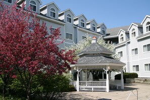 A gazebo with a white roof and white railings, surrounded by trees with pink blossoms.