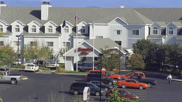 A motel with a row of rooms, a parking lot, and mountains in the background.