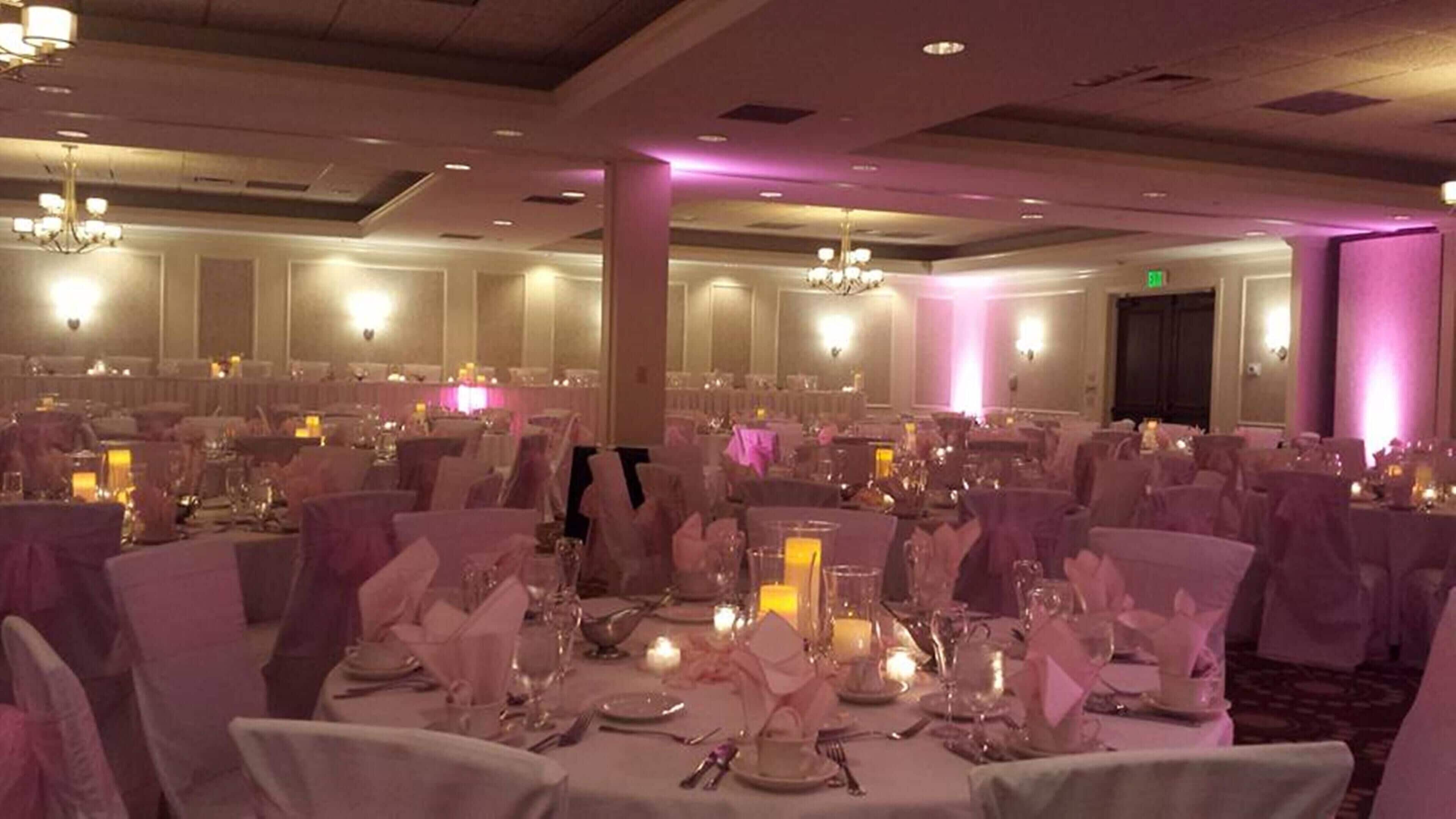 Un salón de banquetes con mesas redondas, sillas, candelabros e iluminación ambiental morada.