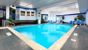 An indoor swimming pool with blue and white walls, a tiled floor, and blue lounge chairs.