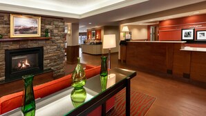 Un hall d’hôtel doté d’une cheminée, d’un comptoir de réception et d’un espace salon avec des coussins rouges.