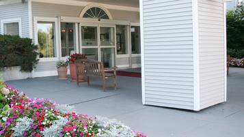 A covered porch with a bench, a potted plant, and a flower bed.