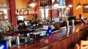 Un bar avec un comptoir en bois, une horloge au mur et diverses bouteilles et verres.