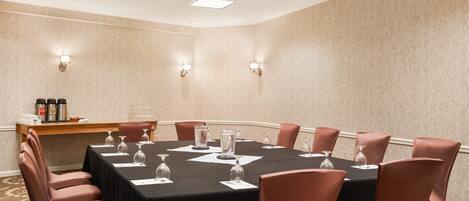 A conference room with a black table, pink chairs, and a wooden side table with bottles.