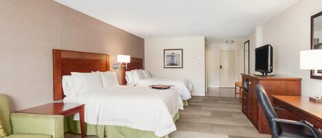 Une chambre d’hôtel comprenant un lit, deux tables de chevet, un bureau, une chaise, un téléviseur et un tableau encadré au mur.