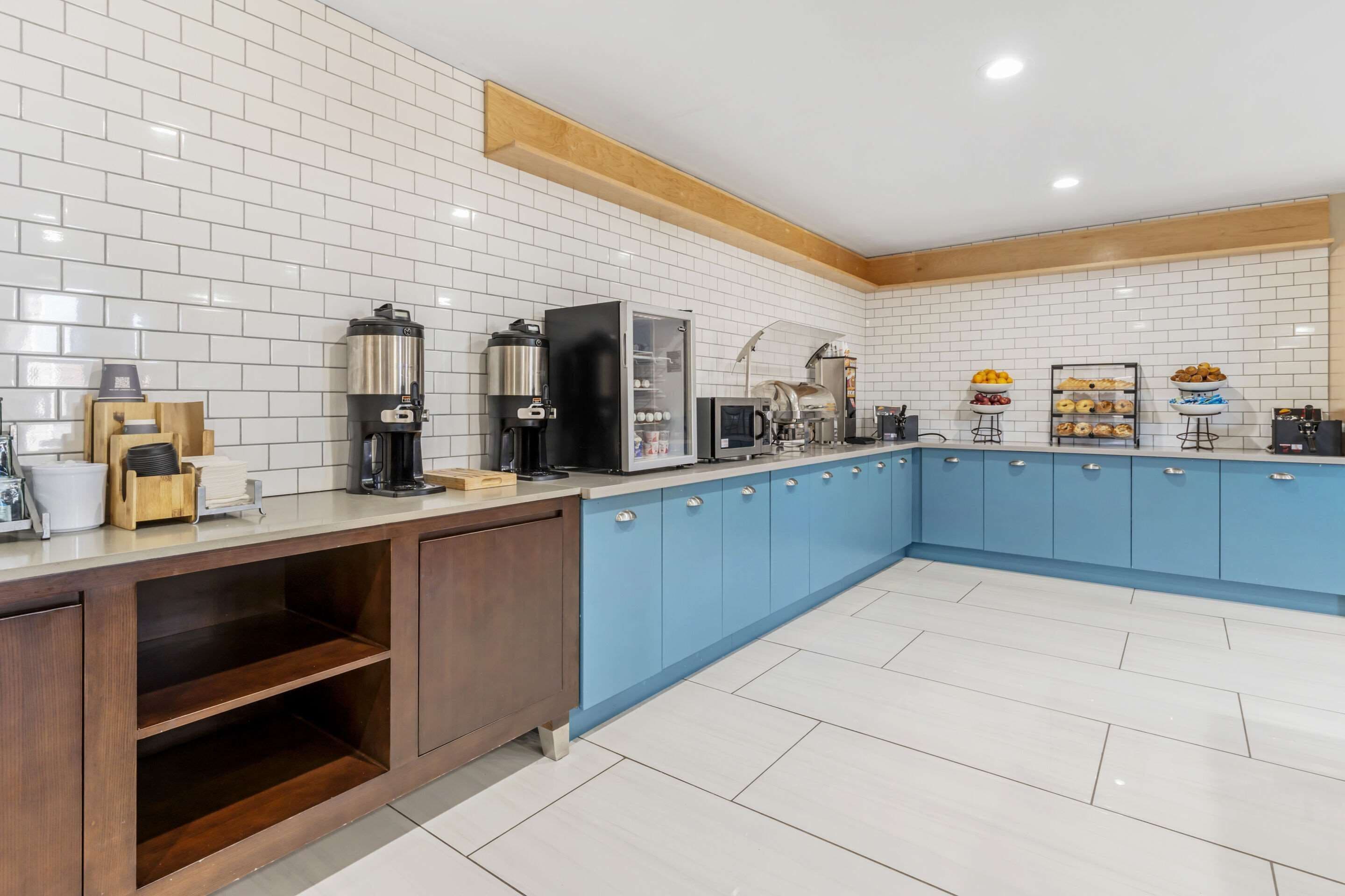 Una cocina moderna con paredes de azulejos blancos, armarios azules y una variedad de electrodomésticos, incluyendo una cafetera y un microondas.