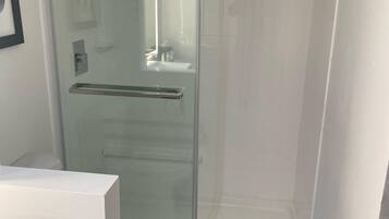 Een moderne badkamer met een glazen douchecabine, toilet en wastafel.