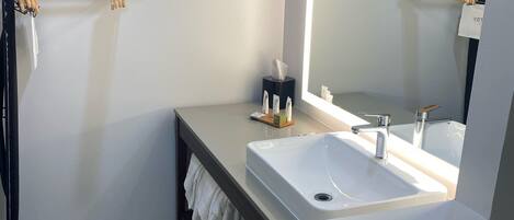 Un baño moderno con un lavamanos blanco, un espejo grande y un perchero para toallas.