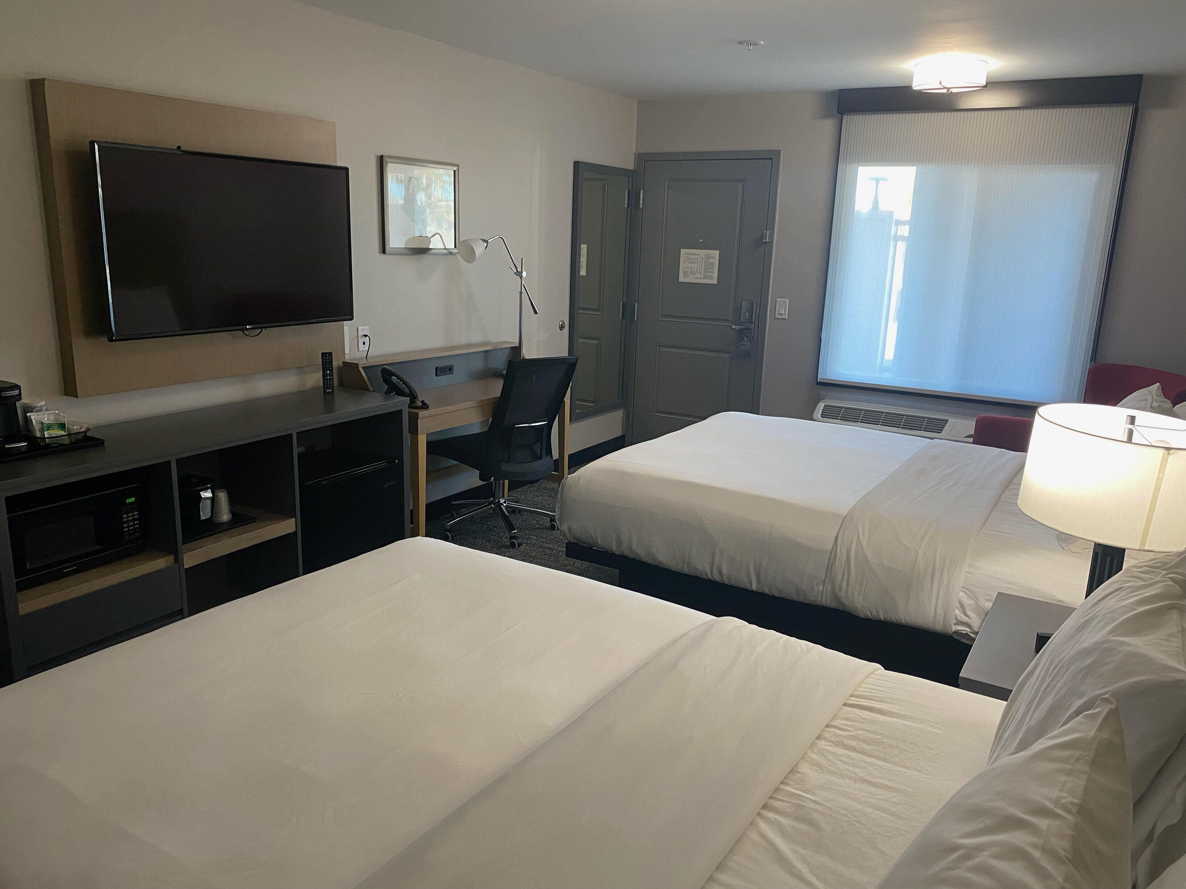 Una habitación de hotel con dos camas, un escritorio con silla, un televisor y una ventana con cortinas.