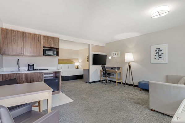A hotel room with a kitchenette, a bed, a desk with a computer, a TV, and a seating area.