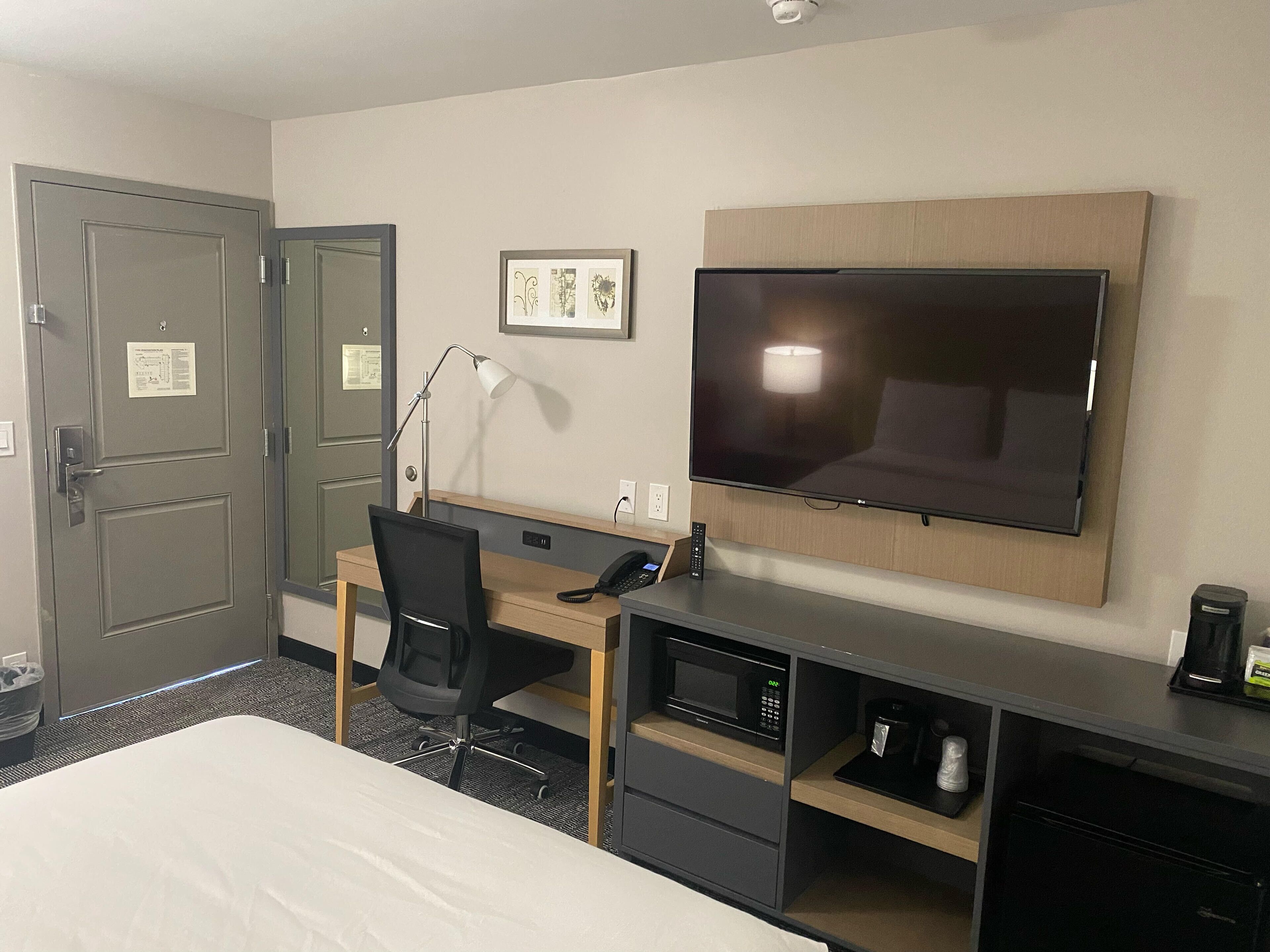 A hotel room with a bed, desk, chair, TV, and a coffee maker.
