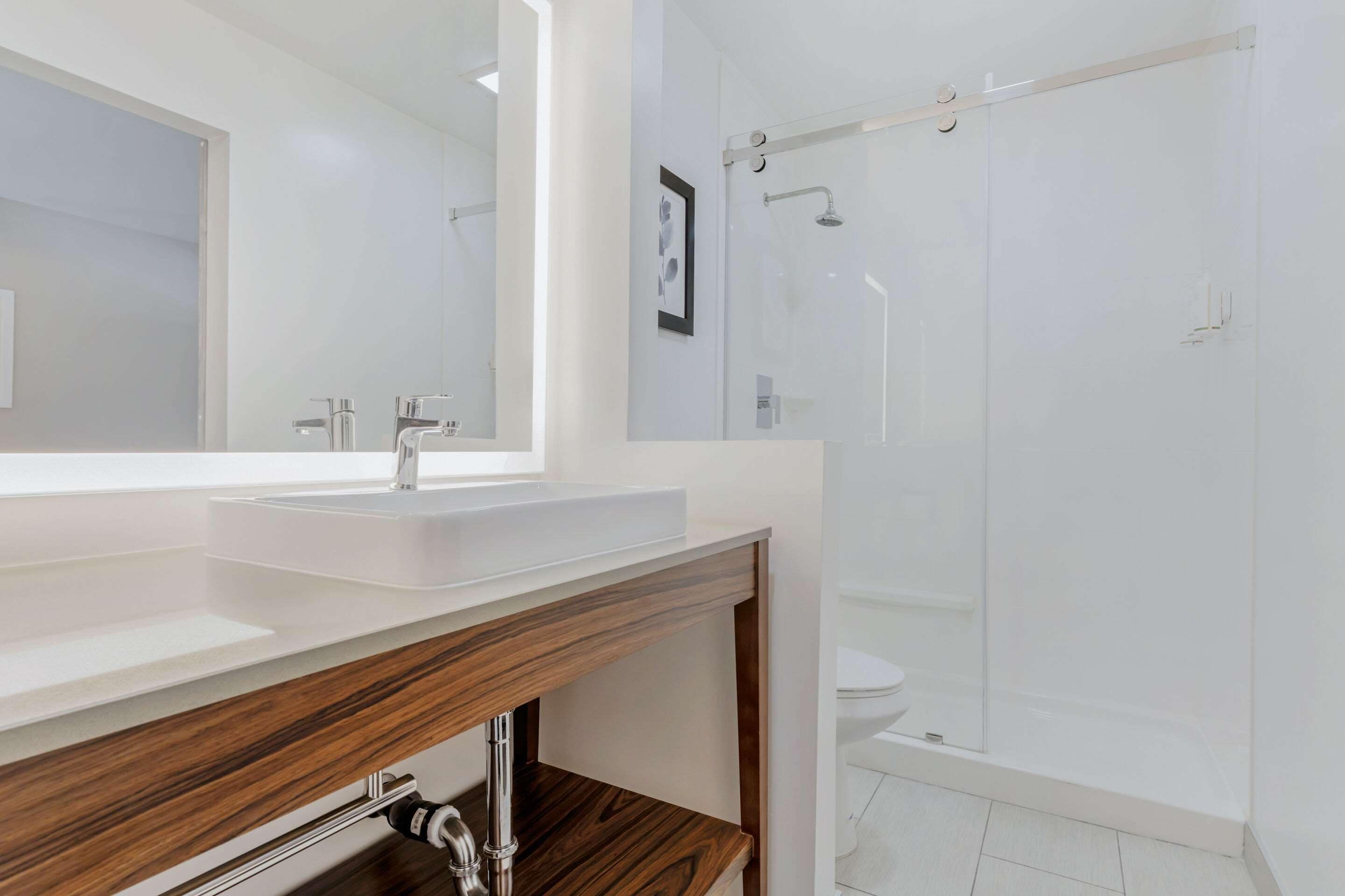 Un baño moderno con tocador de madera, un espejo grande, cabina de ducha y un inodoro.