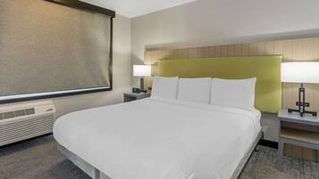 A hotel room with a large bed, two bedside tables, a lamp, a heater, and a window with a view.