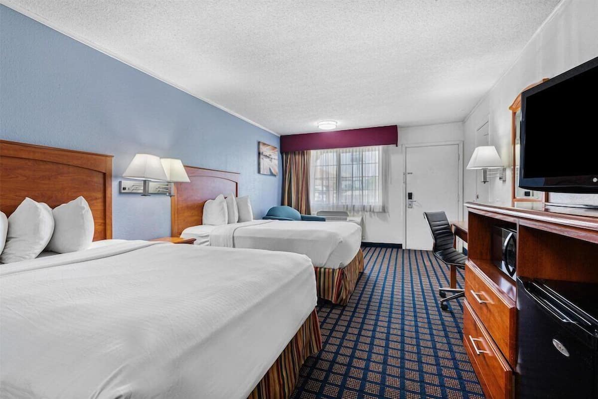 A hotel room with two beds, a desk with a television, and a window with curtains.