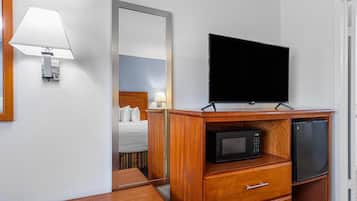 Una habitación de hotel con una cama, un aparador de madera con televisor y microondas, un escritorio y una lámpara de pared.