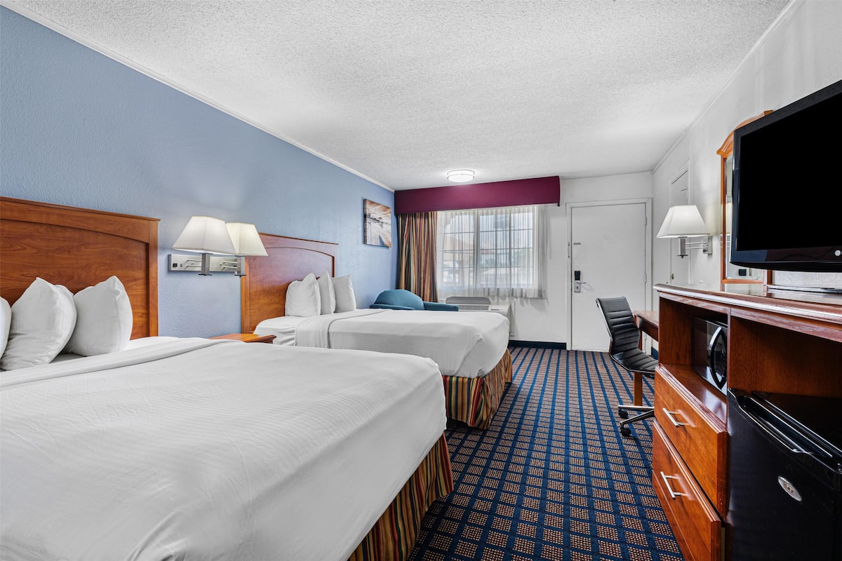 A hotel room with two beds, a desk, a television, and a window with curtains.